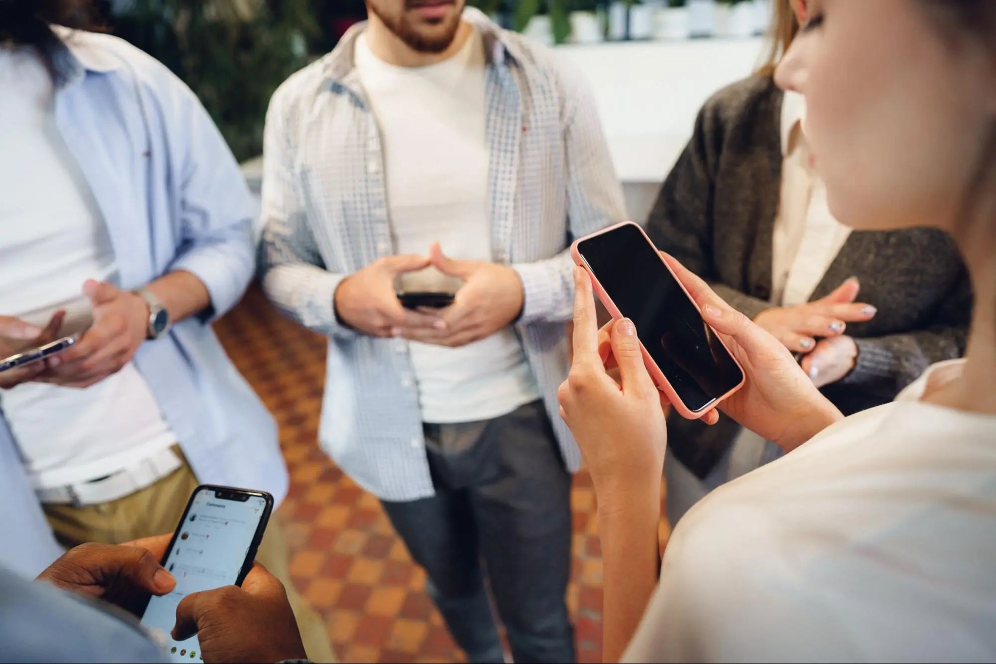 Grupo de pessoas reunidas usando seus smartphones, com destaque em primeiro plano para uma mulher segurando um celular com capinha rosa, ilustrando a expectativa e o uso de novas tecnologias.